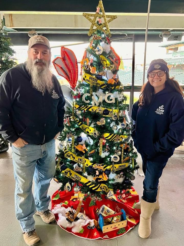 Two CMG employees beside a construction-themed Christmas tree
