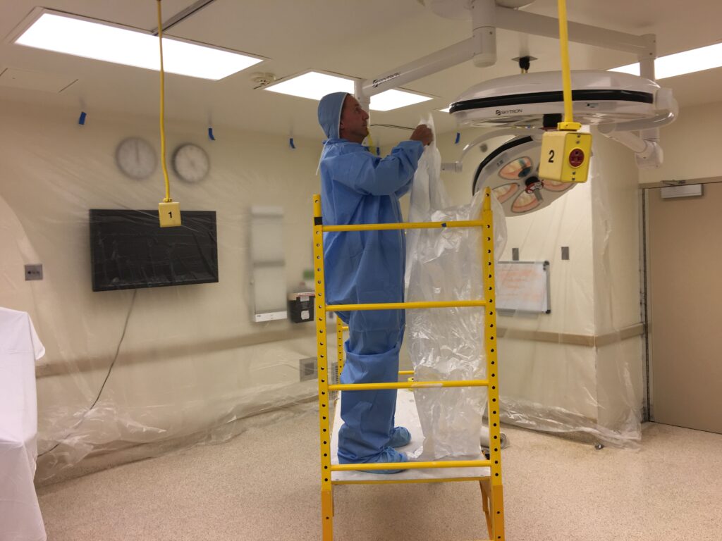 Worker in protective coveralls installing equipment in a medical procedure room